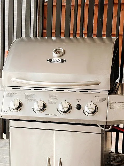 Ground-floor American-style BBQ area, daytime front view of the stainless steel gas grill under its covered patio