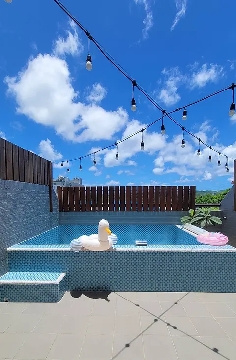 Wide view of the second-floor terrace pool under a blue sky, string lights, and a unicorn-goose float
