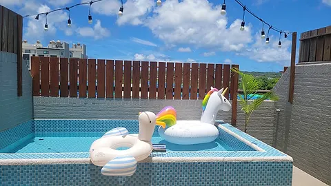 Nikoniko's second-floor terrace pool with blue mosaic tiles, string lights, blue sky and clouds, with swan and unicorn pool floats by the water