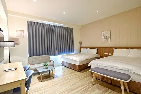 Twin-bed quad room with beige wall paneling, grey curtains, and a grey loveseat