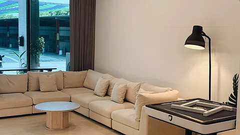 聚會館客廳窗邊角度，米色沙發搭配立燈，後方為落地玻璃門